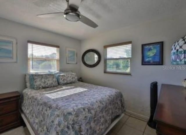 bedroom featuring ceiling fan, baseboards, light tile patterned flooring, and multiple windows