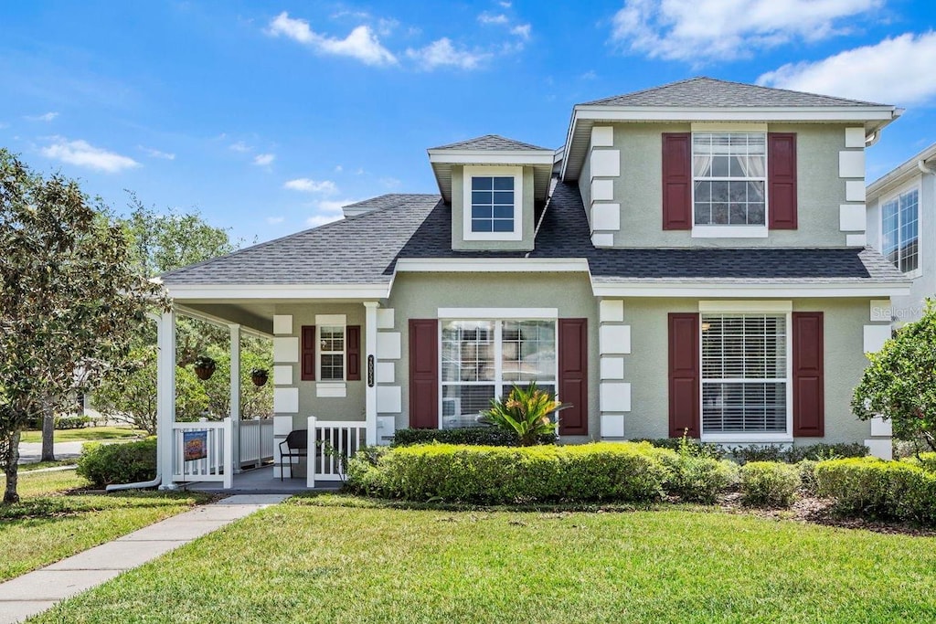 view of front of property featuring a porch, a shingled roof, a front yard, and stucco siding