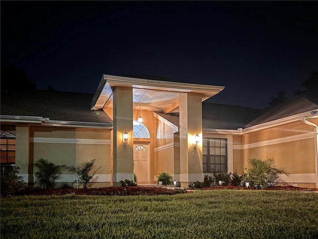 exterior entry at twilight with a lawn and stucco siding