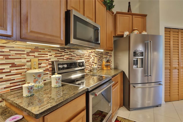 kitchen with dark stone counters, stainless steel appliances, decorative backsplash, and light tile patterned floors