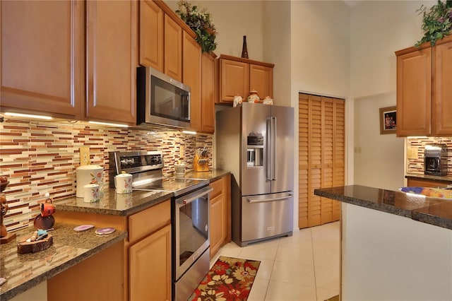 kitchen with decorative backsplash, dark countertops, a high ceiling, appliances with stainless steel finishes, and light tile patterned floors