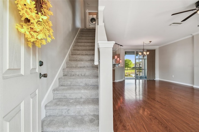 staircase with wood finished floors, washer / dryer, ceiling fan with notable chandelier, baseboards, and crown molding