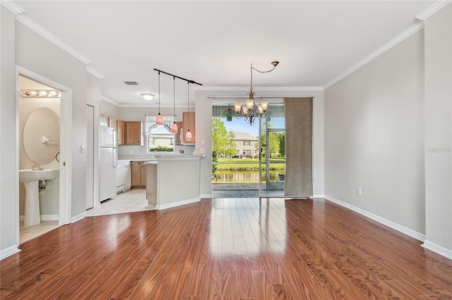 unfurnished living room with an inviting chandelier, ornamental molding, light wood-style flooring, and baseboards