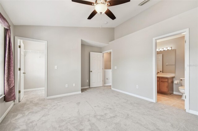 unfurnished bedroom featuring a sink, visible vents, vaulted ceiling, light carpet, and a spacious closet