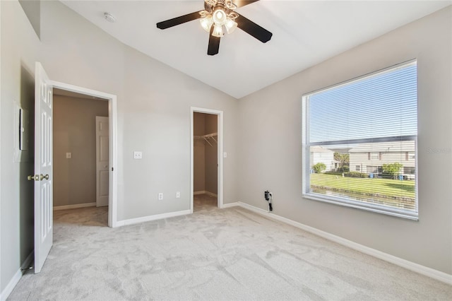 unfurnished bedroom featuring a ceiling fan, light carpet, baseboards, lofted ceiling, and a spacious closet