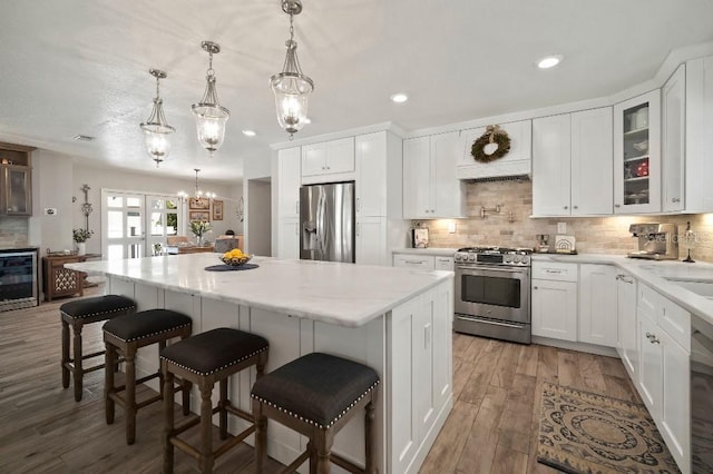 kitchen featuring an inviting chandelier, a center island, appliances with stainless steel finishes, wood finished floors, and beverage cooler