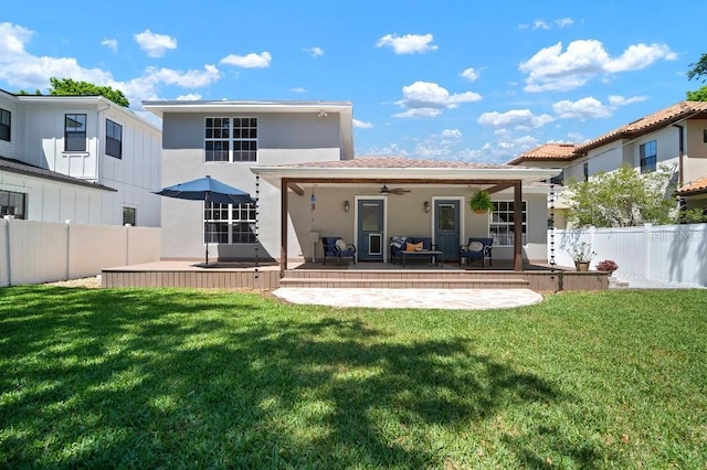 back of property with stucco siding, a fenced backyard, a ceiling fan, and a lawn