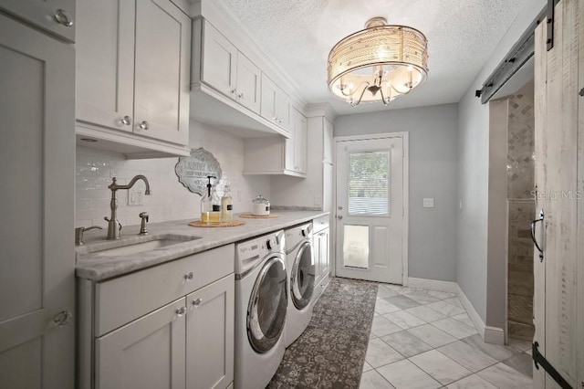 clothes washing area with a textured ceiling, washing machine and clothes dryer, a sink, an inviting chandelier, and cabinet space