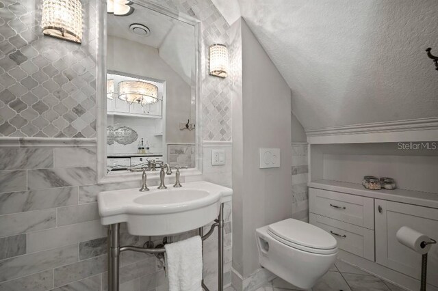 bathroom featuring lofted ceiling, toilet, marble finish floor, and tile walls