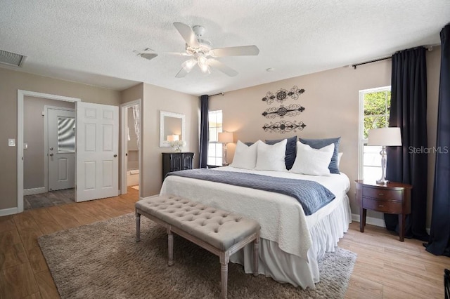 bedroom featuring light wood-style floors, ceiling fan, baseboards, visible vents, and a textured ceiling