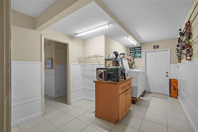 laundry room featuring washing machine and clothes dryer, light tile patterned flooring, laundry area, a textured ceiling, and a wainscoted wall