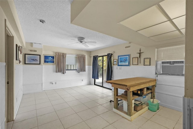 interior space with a wainscoted wall, cooling unit, a ceiling fan, and a textured ceiling