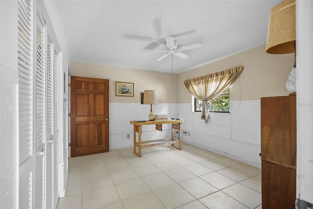 interior space with a ceiling fan, a textured ceiling, and wainscoting