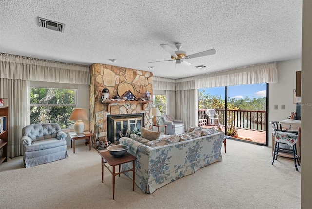living area with visible vents, a ceiling fan, a stone fireplace, a textured ceiling, and carpet flooring