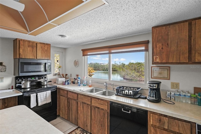 kitchen featuring brown cabinetry, a sink, light countertops, light tile patterned floors, and black appliances