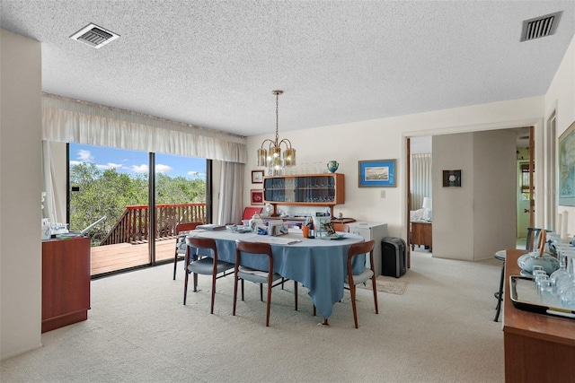 carpeted dining room featuring a notable chandelier, a textured ceiling, and visible vents