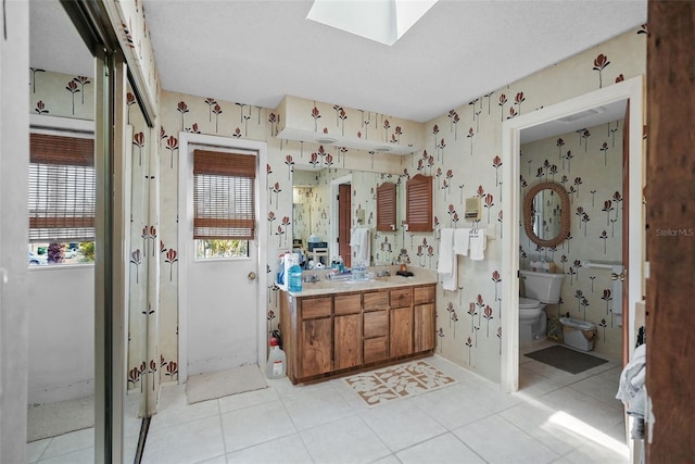 full bathroom featuring vanity, tile patterned flooring, toilet, wallpapered walls, and a skylight