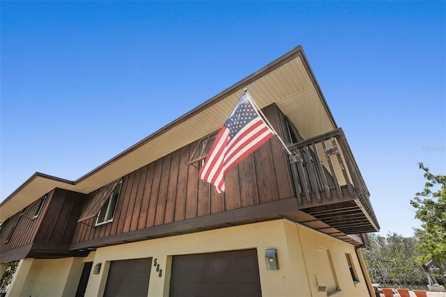 view of side of property with stucco siding, an attached garage, and a balcony