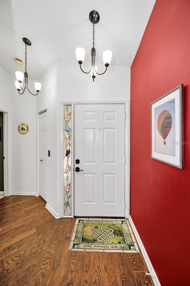 entrance foyer featuring baseboards, a textured ceiling, wood finished floors, and a notable chandelier