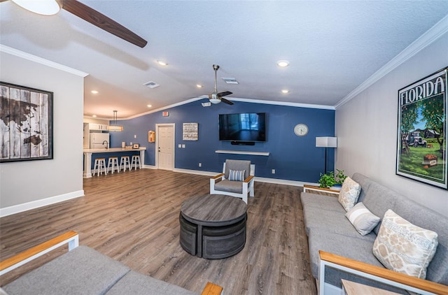 living area featuring a ceiling fan, vaulted ceiling, ornamental molding, and wood finished floors