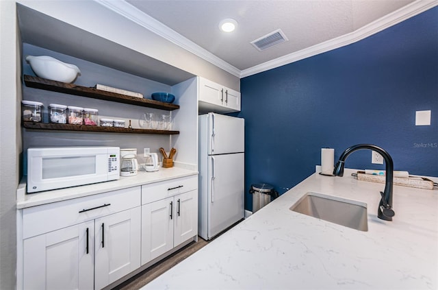 kitchen with crown molding, a sink, white appliances, white cabinetry, and visible vents