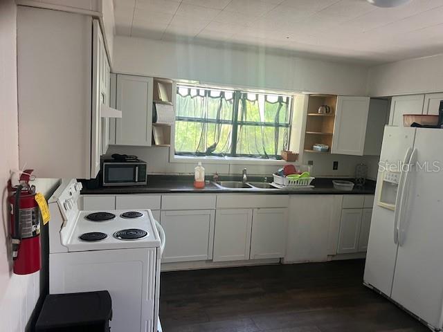 kitchen with a sink, open shelves, white appliances, dark countertops, and dark wood finished floors