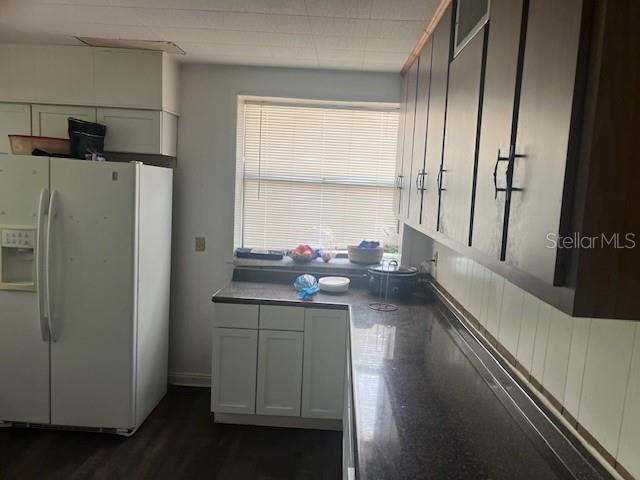 kitchen with dark countertops, white fridge with ice dispenser, and dark wood-type flooring