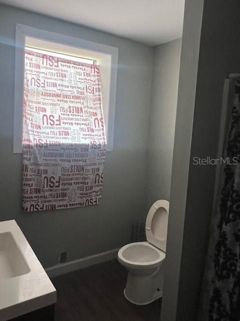 bathroom featuring baseboards, wood finished floors, toilet, and vanity