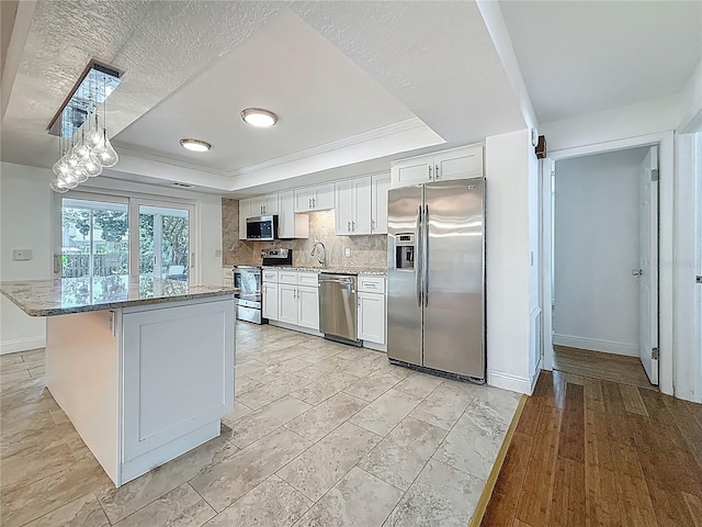 13891 Feather Sound Dr, Clearwater, FL 33762 - kitchen featuring appliances with stainless steel finishes, a raised ceiling, white cabinets, light stone counters, and a center island