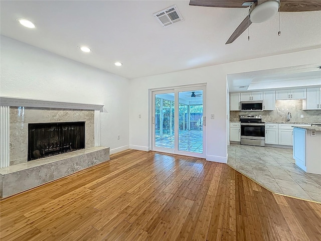 13891 Feather Sound Dr, Clearwater, FL 33762 - unfurnished living room featuring a ceiling fan, light wood-style flooring, recessed lighting, and a premium fireplace
