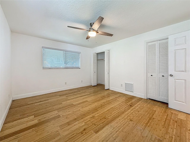 13891 Feather Sound Dr, Clearwater, FL 33762 - unfurnished bedroom with two closets, light wood-style floors, a ceiling fan, and a textured ceiling