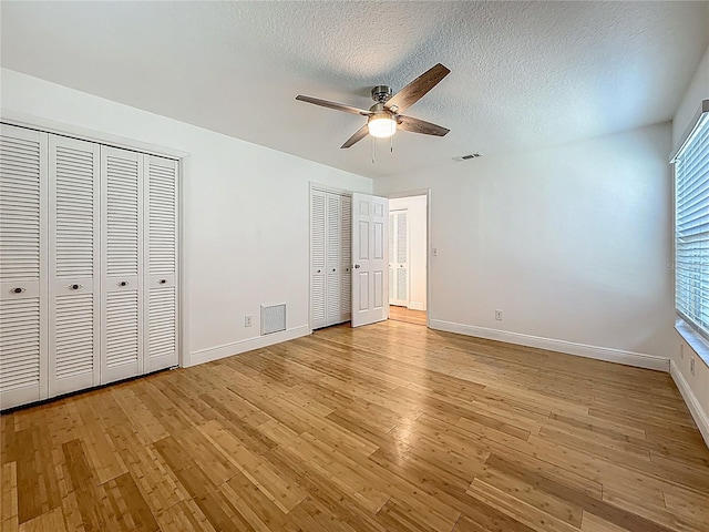 13891 Feather Sound Dr, Clearwater, FL 33762 - unfurnished bedroom with multiple closets, light wood-style flooring, a textured ceiling, and a ceiling fan