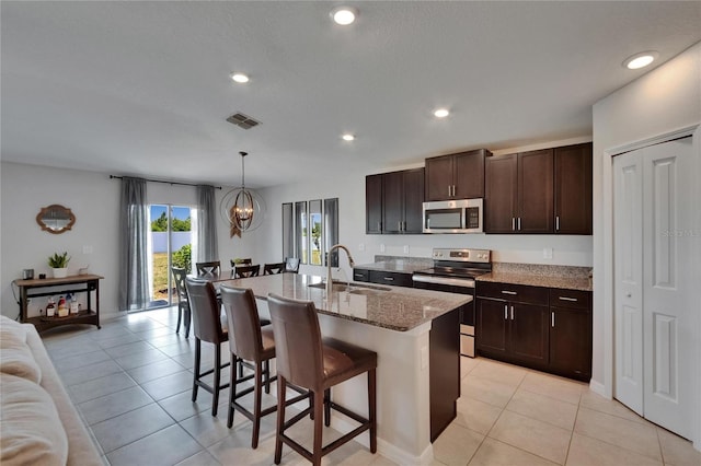 13506 Wild Ginger St, Riverview, FL 33579 - kitchen with stainless steel appliances, a breakfast bar, light tile patterned flooring, dark brown cabinets, and light stone counters