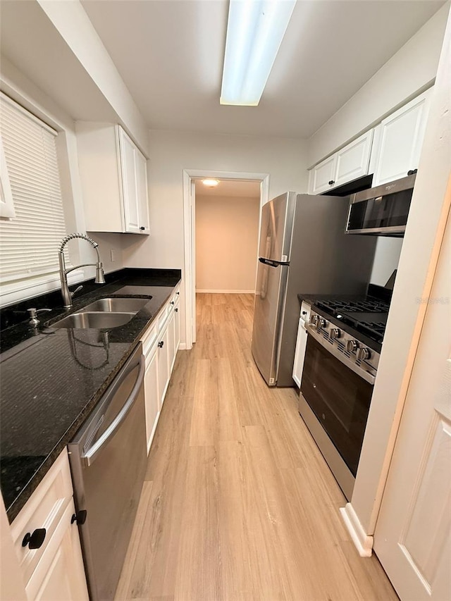 1505 Piedmont Dr, Deltona, FL 32725 - kitchen featuring appliances with stainless steel finishes, a sink, light wood finished floors, white cabinetry, and dark stone counters