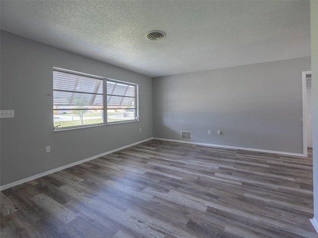 empty room with baseboards, wood finished floors, visible vents, and a textured ceiling