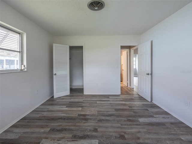 unfurnished bedroom with dark wood-style flooring, baseboards, multiple windows, and visible vents