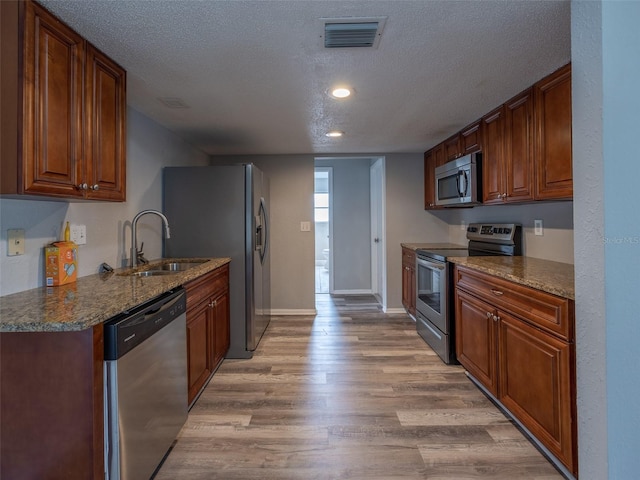 kitchen featuring light wood-style flooring, a sink, a textured ceiling, visible vents, and appliances with stainless steel finishes