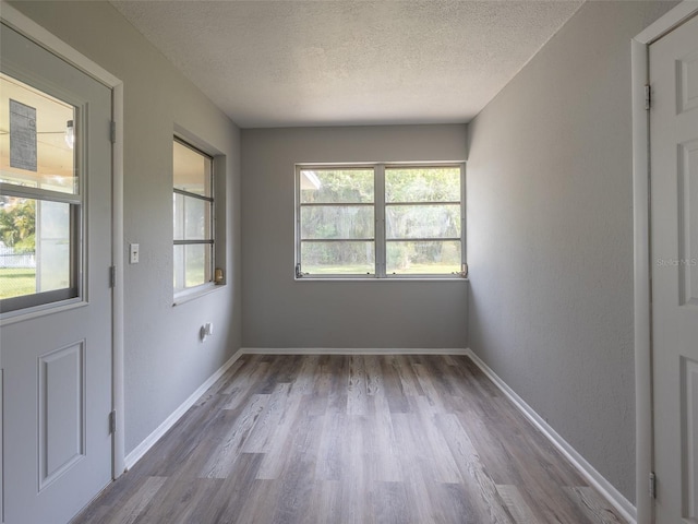 empty room with wood finished floors, a textured ceiling, and baseboards