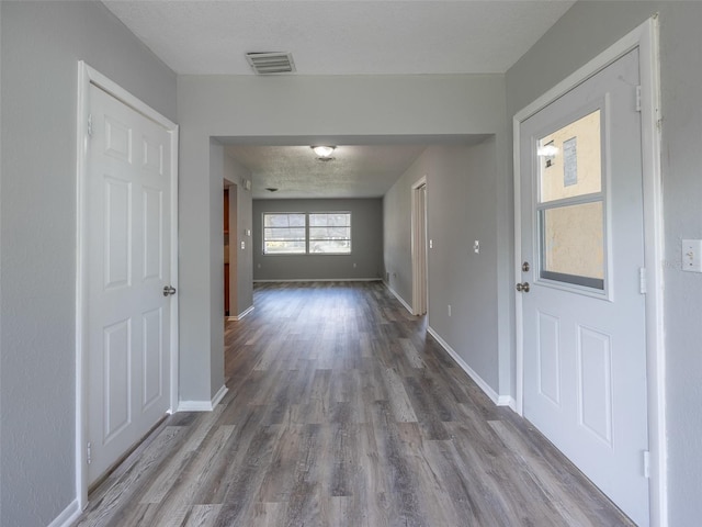 hall with baseboards, wood finished floors, and visible vents