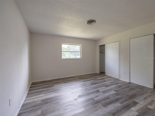 unfurnished bedroom featuring visible vents, wood finished floors, a textured ceiling, and two closets