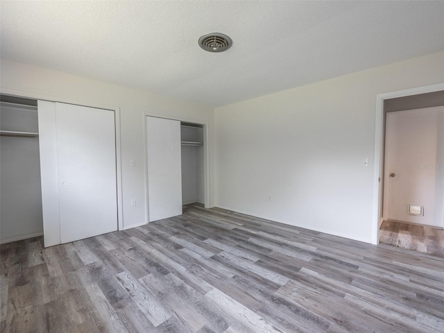 unfurnished bedroom featuring two closets, wood finished floors, visible vents, and a textured ceiling