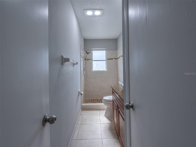 bathroom with tile patterned floors, a textured ceiling, toilet, tiled shower, and baseboards