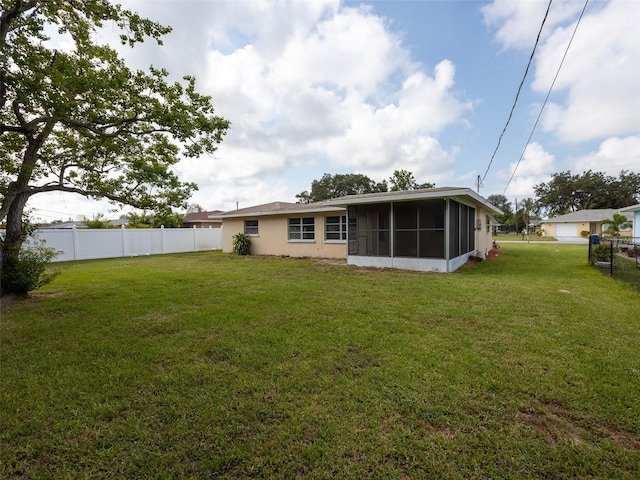 back of house featuring a lawn, a sunroom, a fenced backyard, and stucco siding