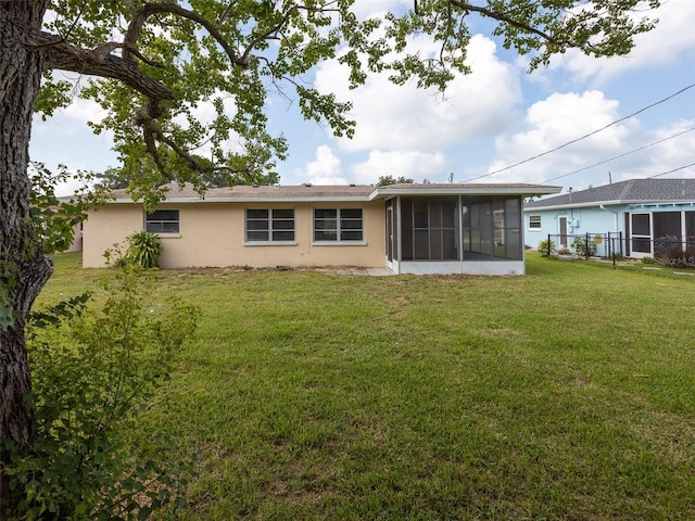 rear view of property featuring a sunroom, fence, stucco siding, and a lawn