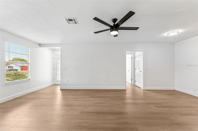 empty room featuring light wood-type flooring, a textured ceiling, visible vents, and a ceiling fan