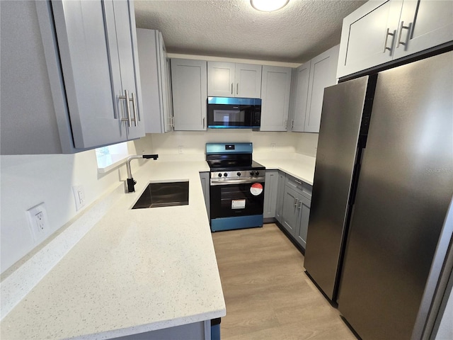 kitchen featuring a sink, stainless steel appliances, a textured ceiling, gray cabinetry, and light wood-style floors