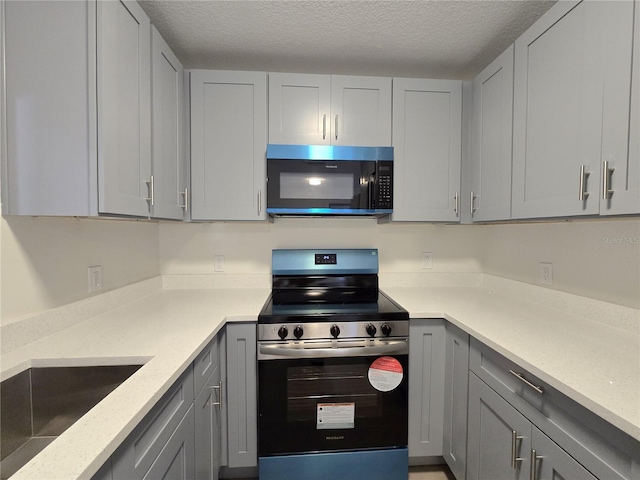 kitchen featuring a textured ceiling, light stone counters, appliances with stainless steel finishes, and gray cabinets