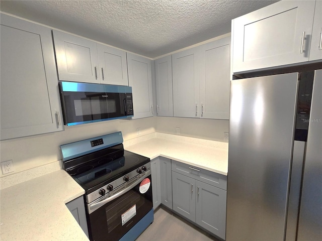 kitchen with a textured ceiling, gray cabinets, and appliances with stainless steel finishes