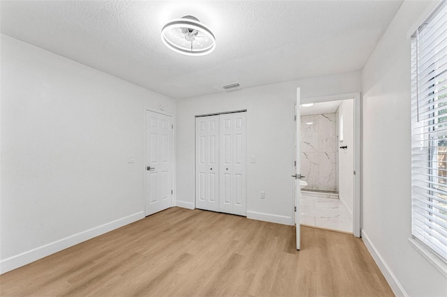 unfurnished bedroom with multiple windows, light wood-style floors, baseboards, and a textured ceiling