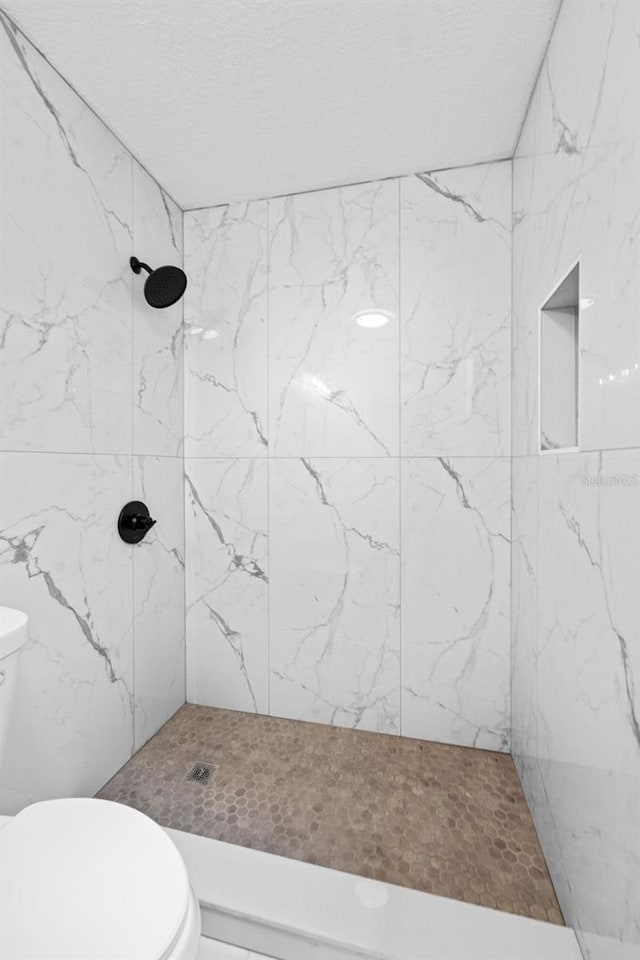 full bath with toilet, a textured ceiling, and a tile shower